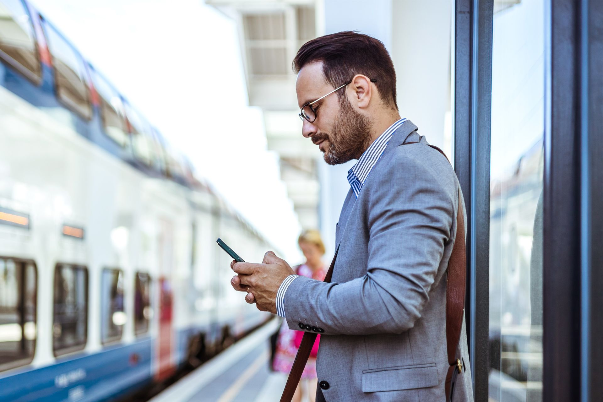 Man in suit at train platform looking at his phone. Train in background.