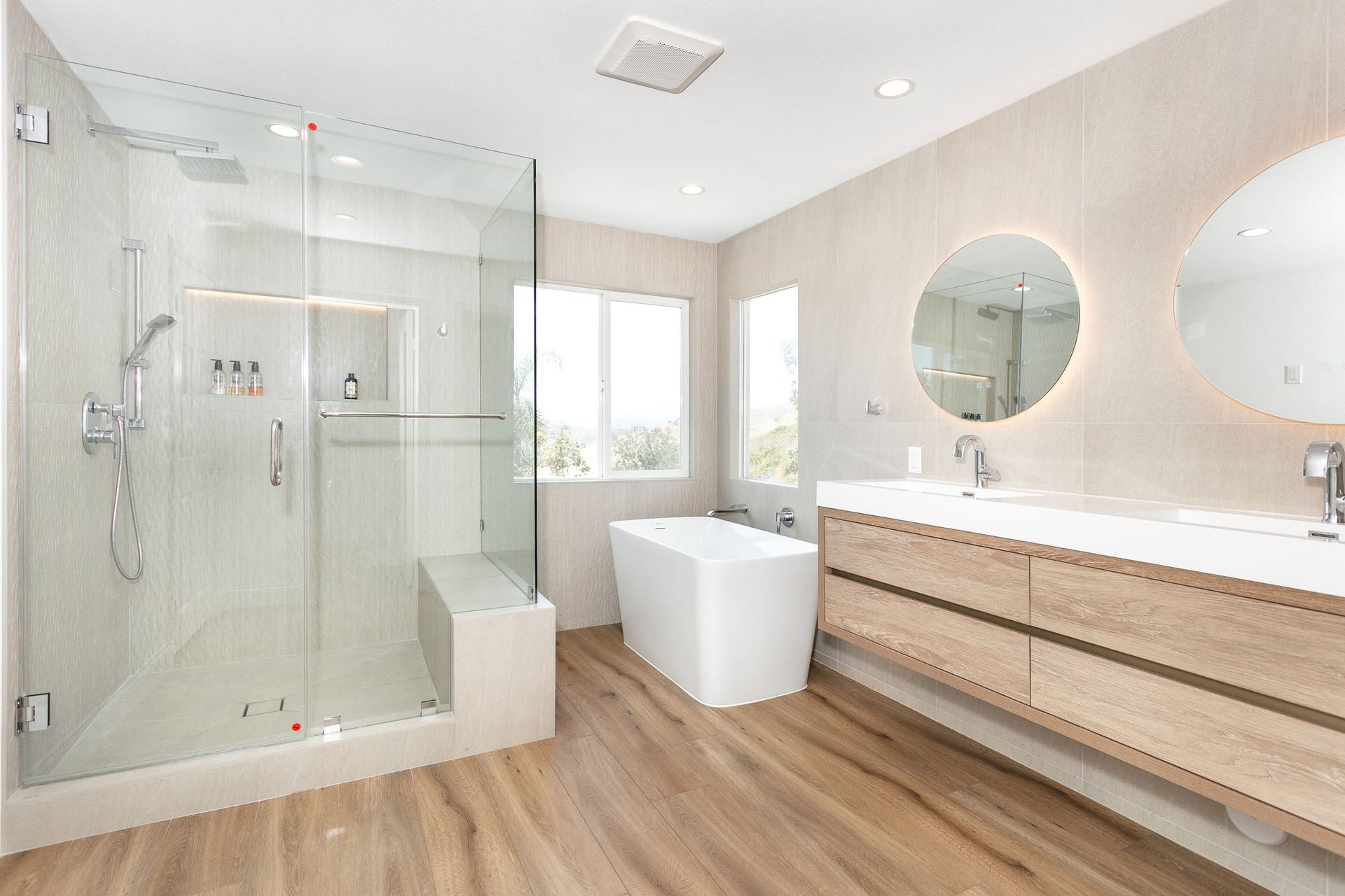 Modern bathroom with glass shower, soaking tub, double vanity, and natural wood flooring.