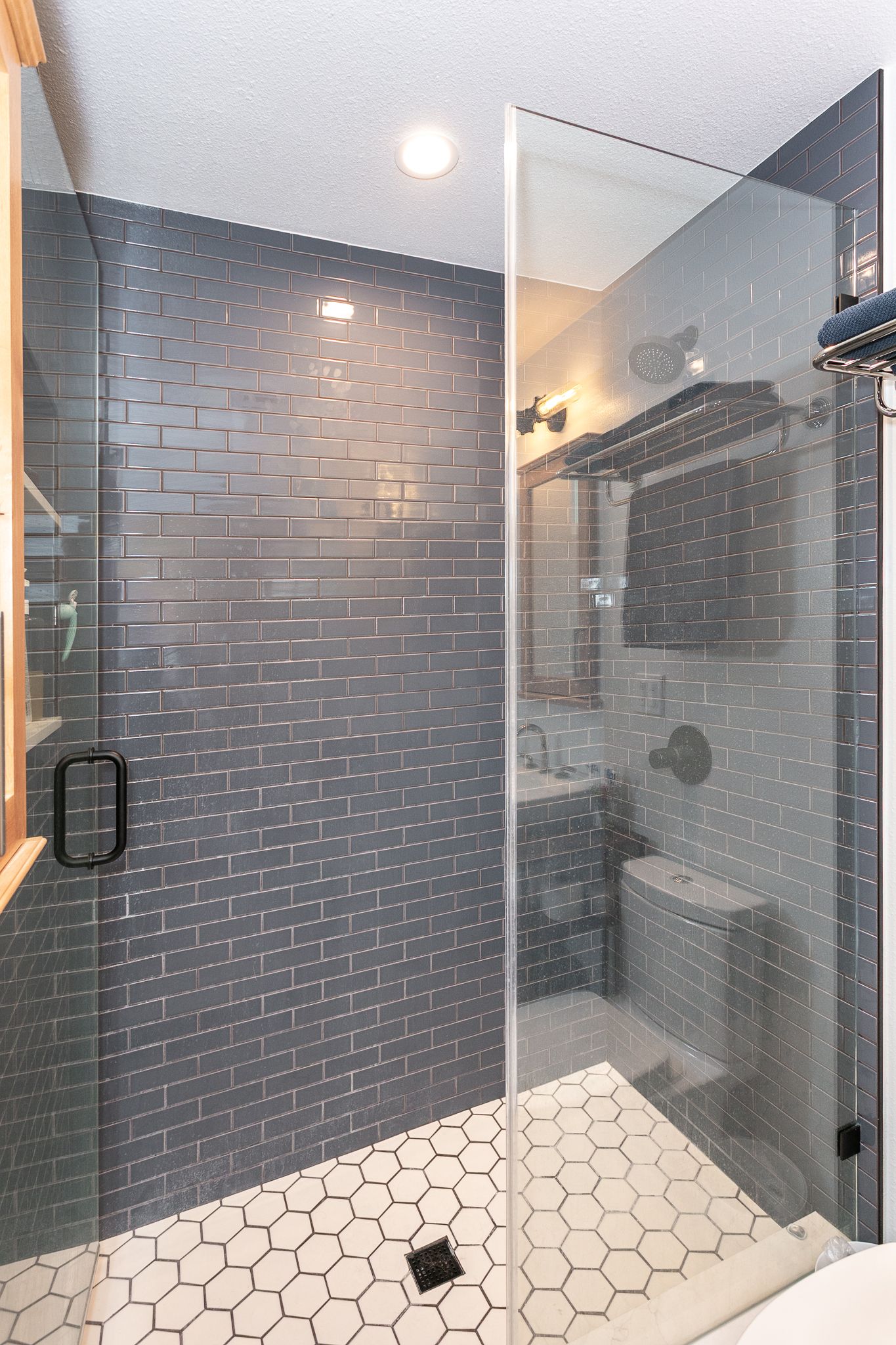 Small master bathroom with a custom tile shower, a shampoo niche with quartz shelving, a frameless shower door with black hardware, and black showerhead trims.