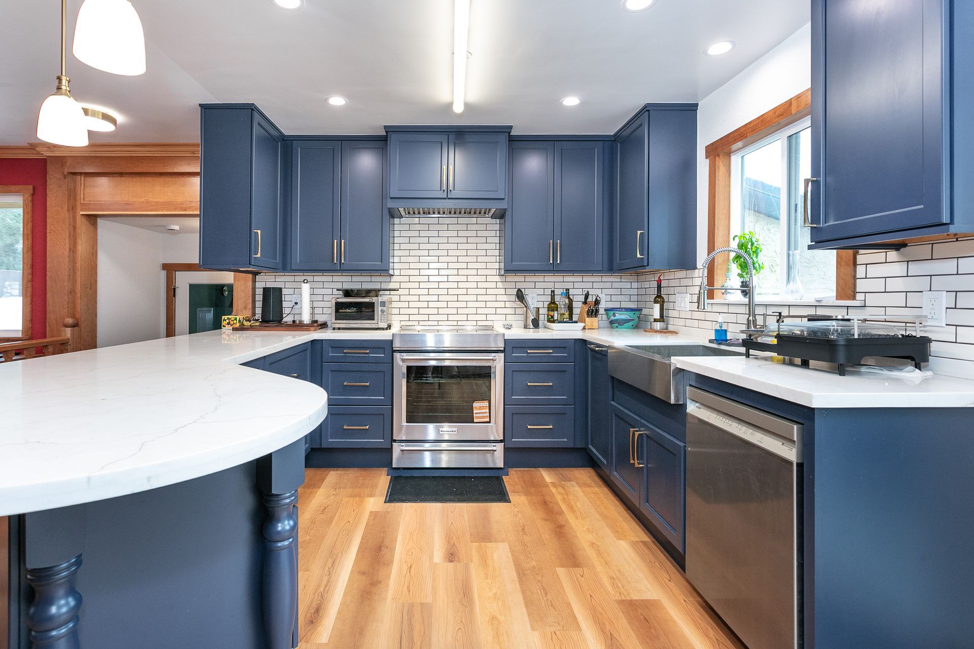 Blue kitchen with white countertops, stainless steel appliances, and hardwood floors.