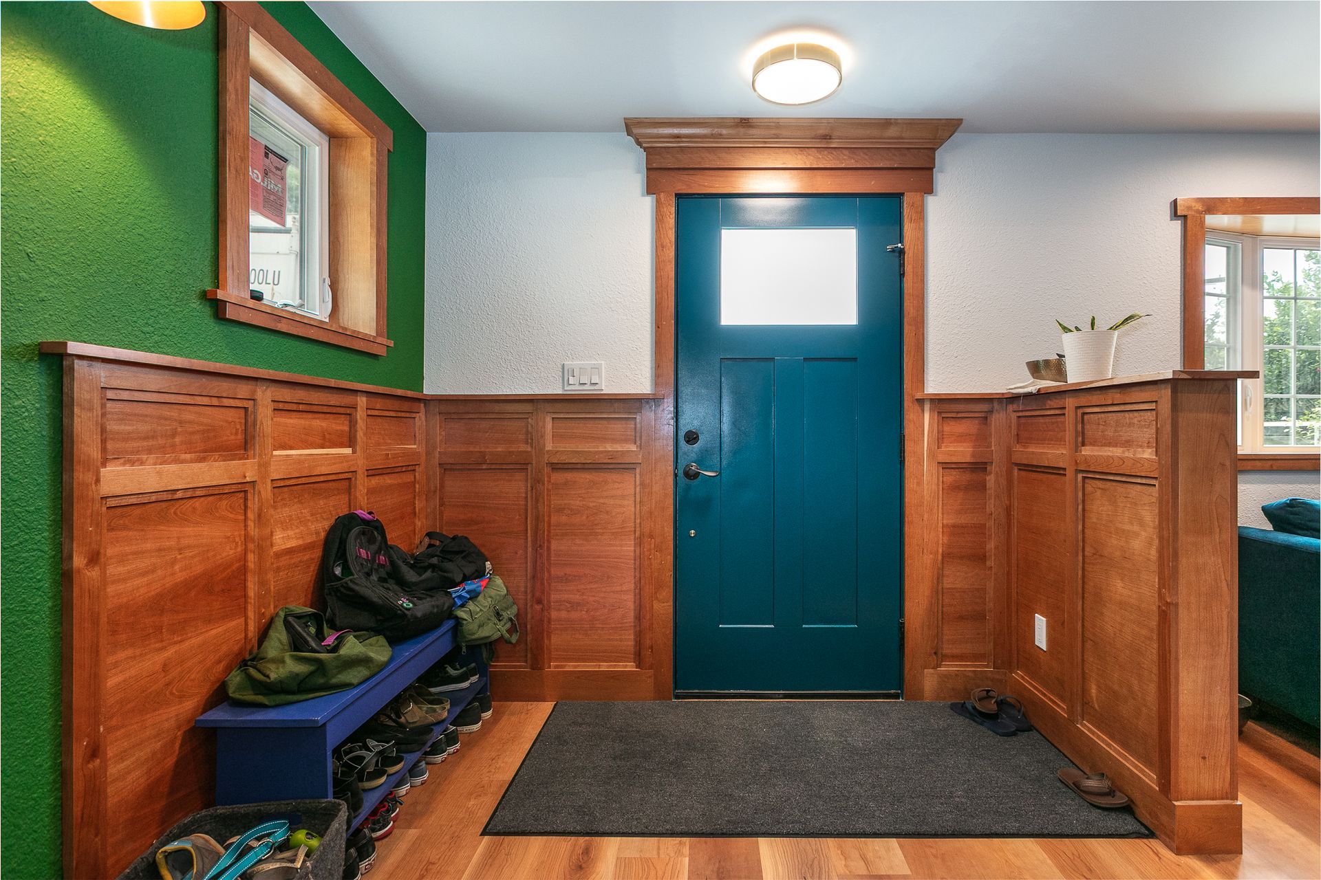 Entryway with teal door, wood paneling, blue bench, and green wall.