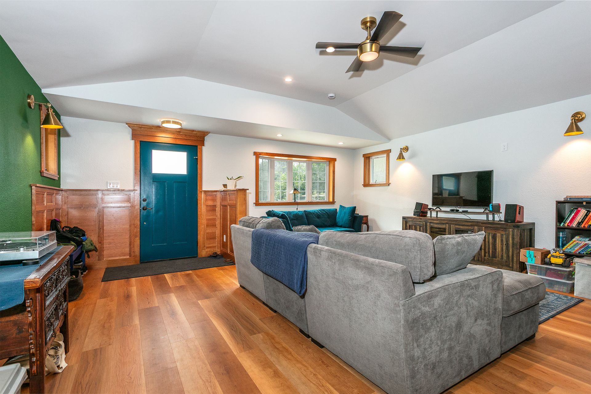 Living room with wood floors, blue door, gray couch, and TV.