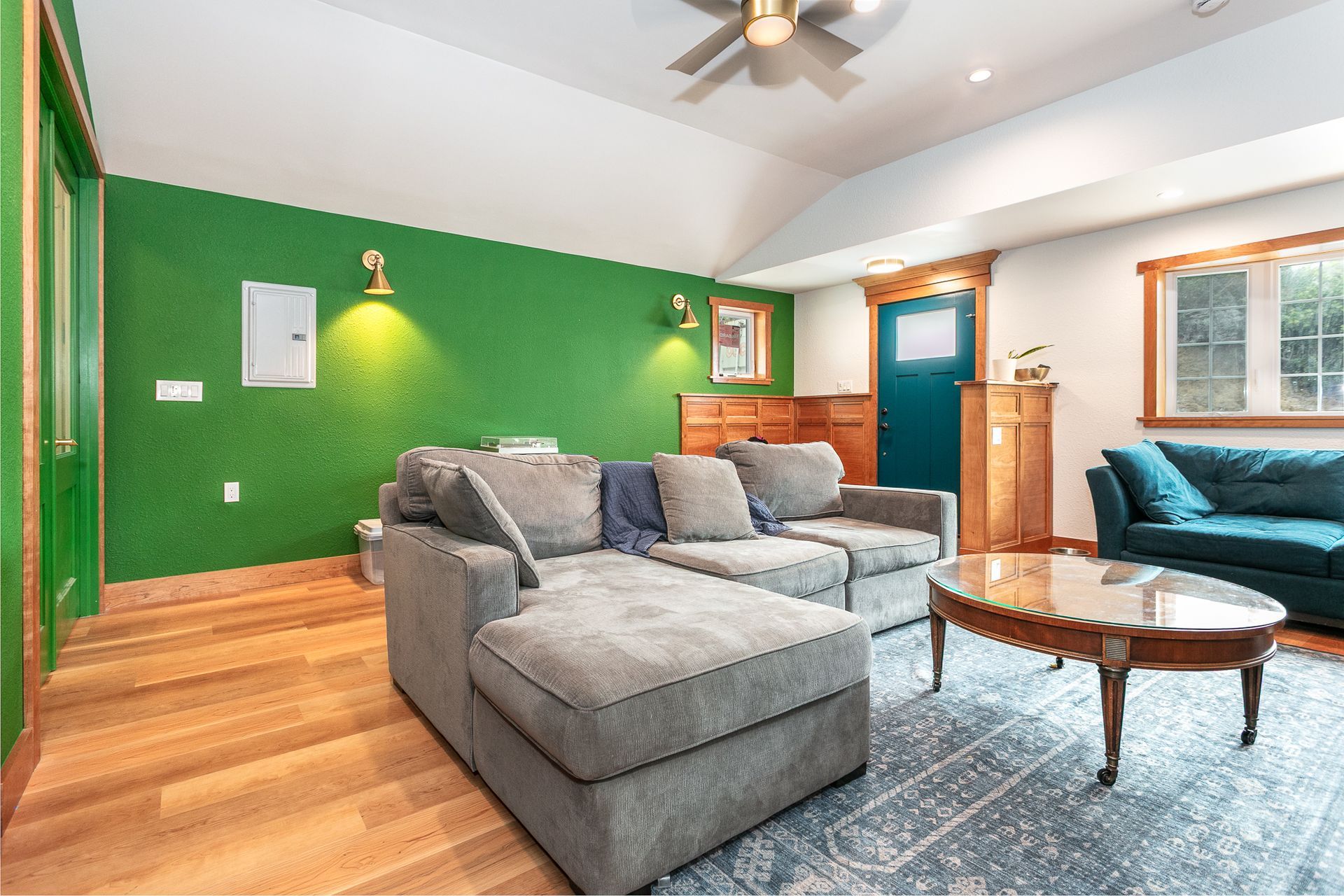 A cozy living room with green walls, gray sectional sofa, coffee table, and a blue sofa.