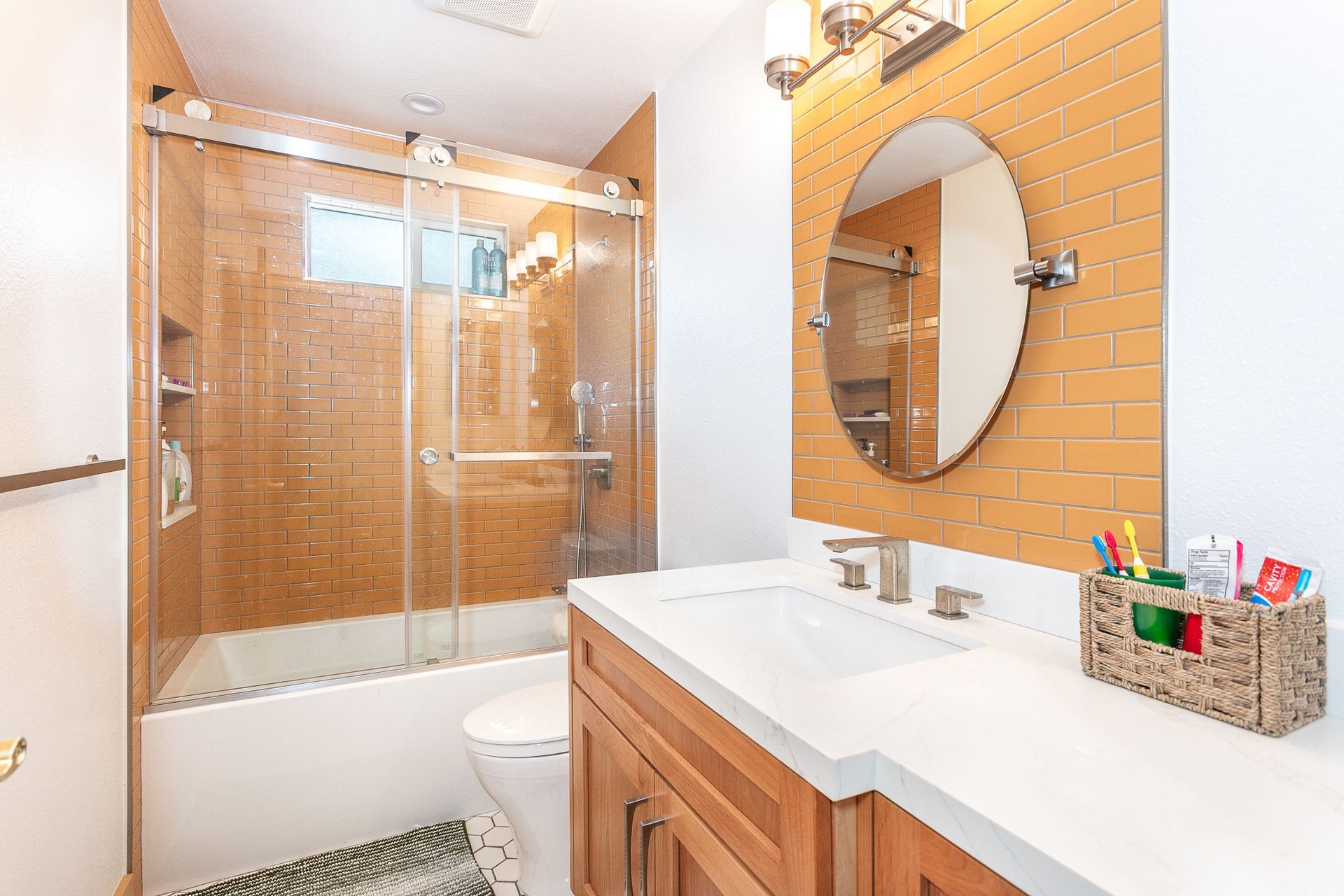 Guest bathroom remodel featuring a custom ceramic orange tile for the tub walls and behind the vanity mirror. A custom-built floating vanity and a frameless shower/tub sliding door.