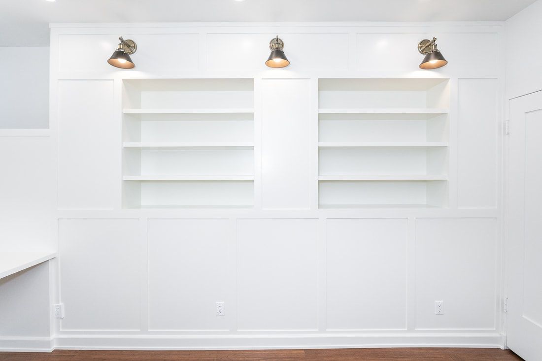 White built-in shelves with three sconce lights, set into a white paneled wall.