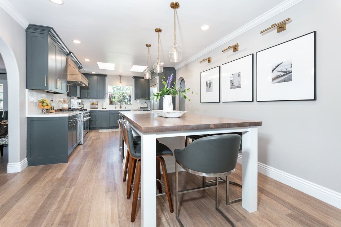 Modern kitchen with gray cabinets, wooden floor, large island table, and three framed pictures.