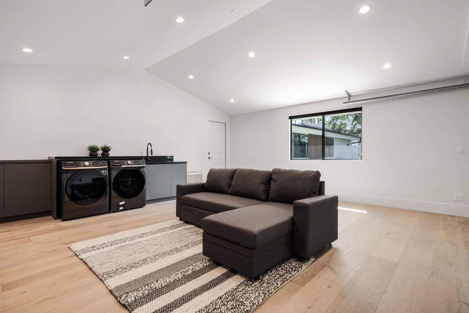 Modern laundry room with sofa, washer/dryer, and rug on hardwood floor.