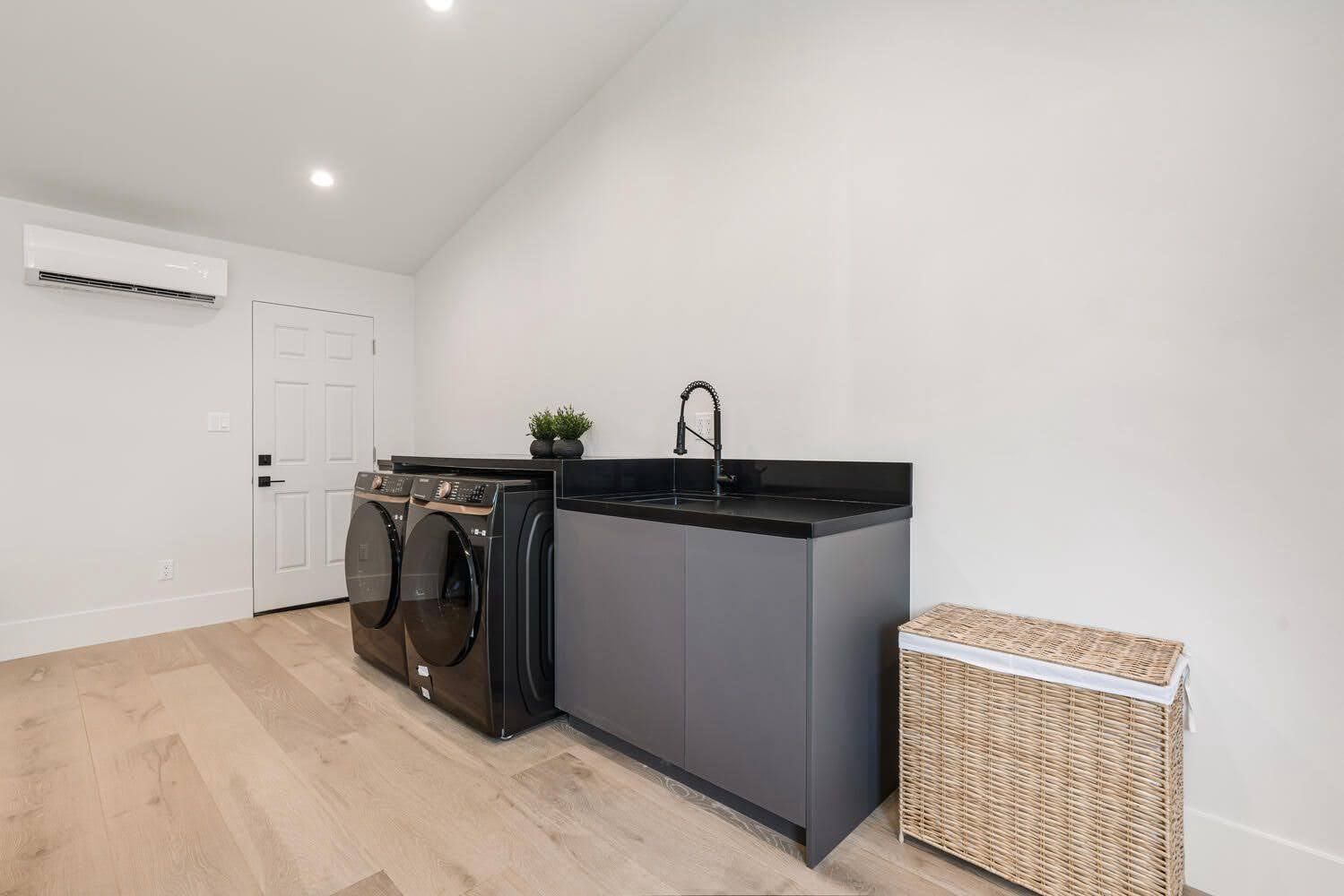 A laundry room with a black washer and dryer, sink, and wicker hamper.