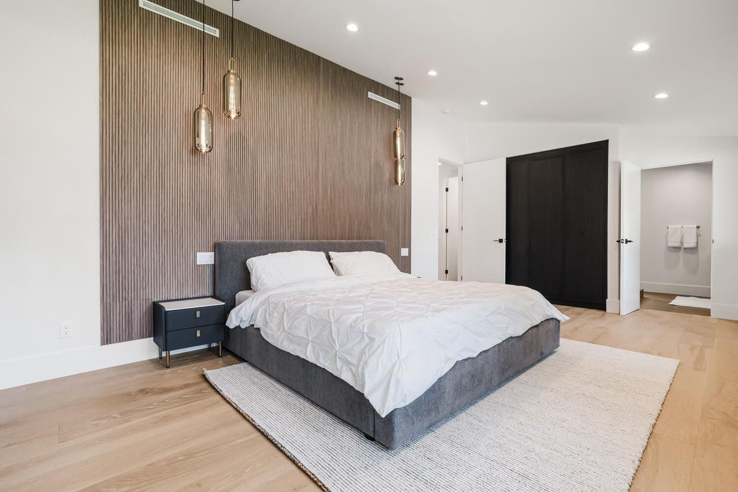 Modern bedroom with bed, rug, and hanging lights against a patterned accent wall.