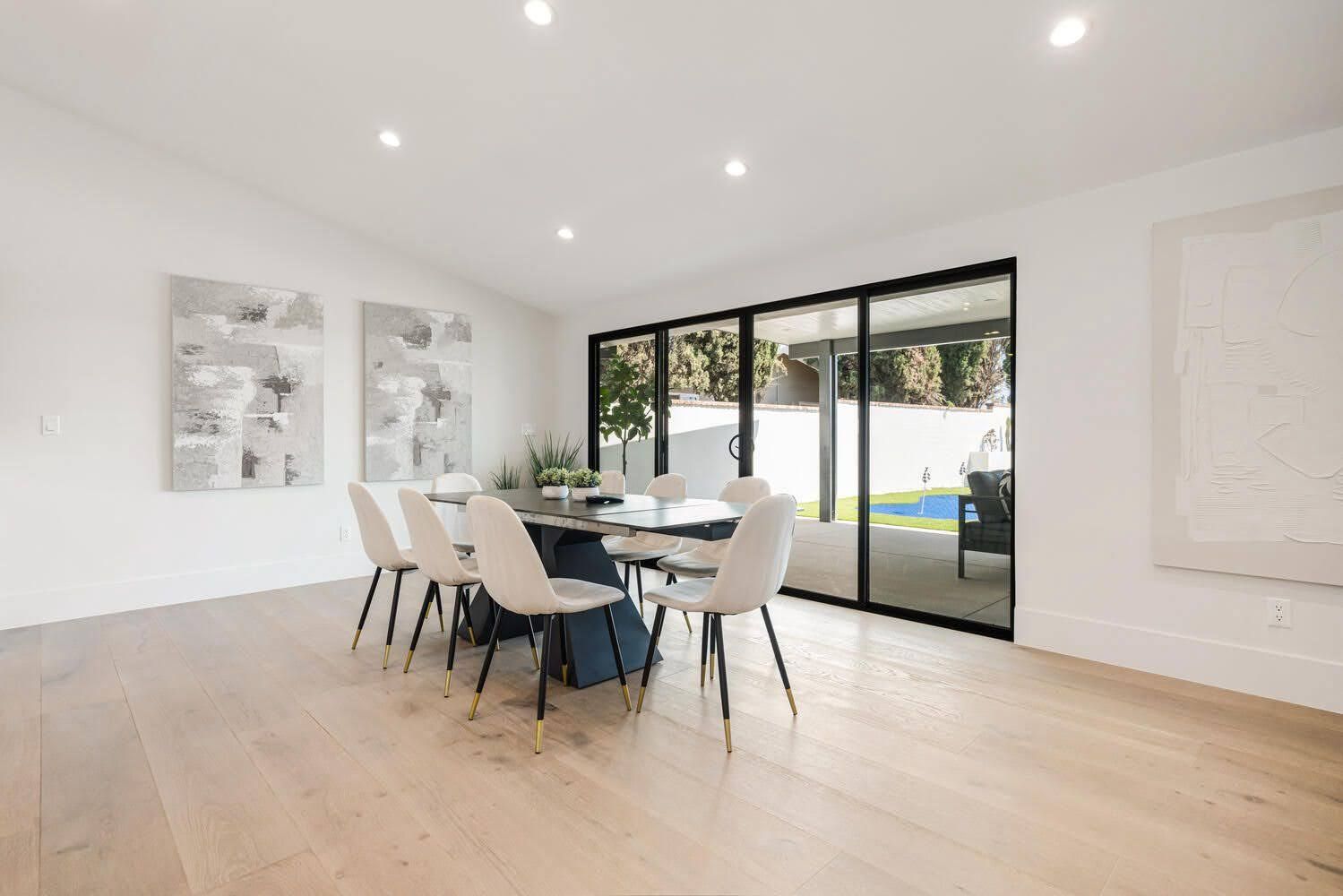 Modern dining room with a dark table, white chairs, and sliding glass doors.