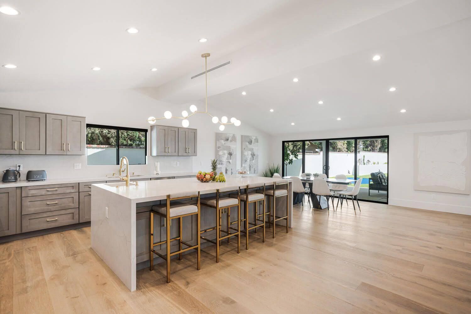 Modern open kitchen with a large island, wood floors, and dining area, connected to an outdoor space.