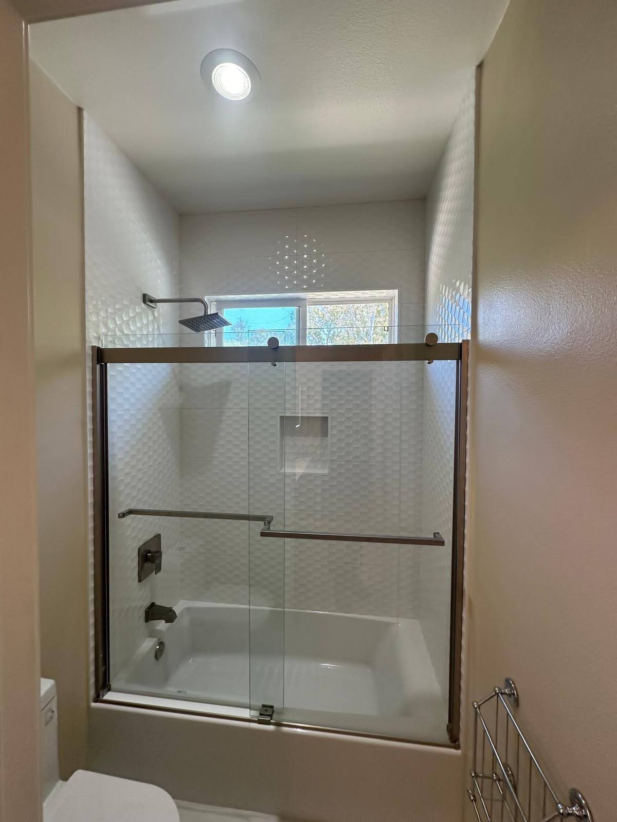 Bathroom with a tub, glass shower doors, and white tile.