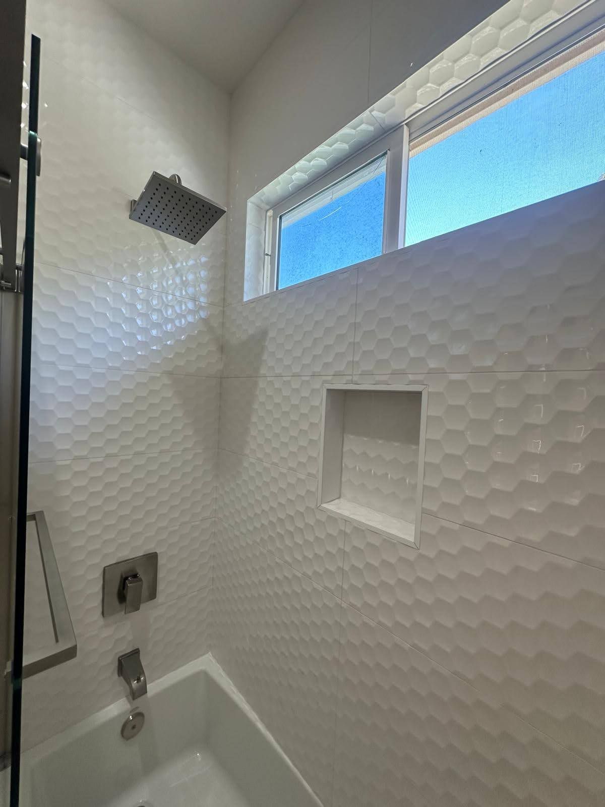 White tiled shower with built-in shelf, square shower head, and window.