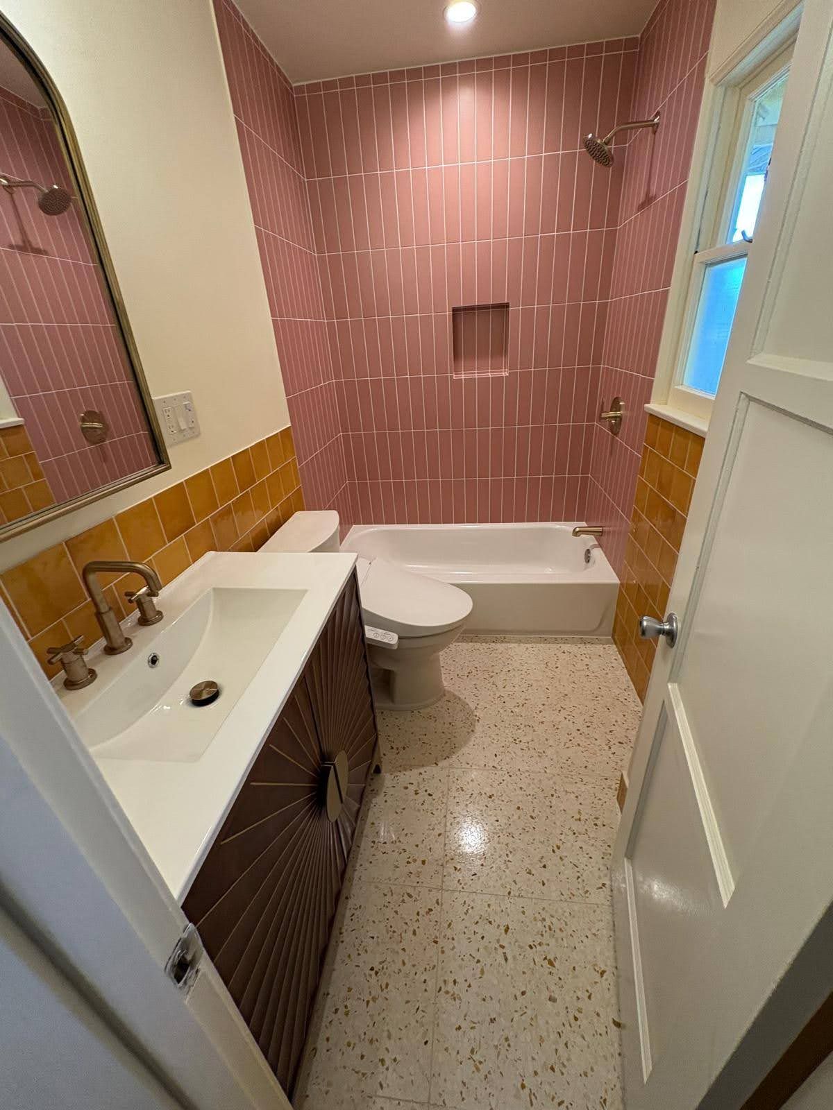 Bathroom with pink tiled shower, yellow accent tiles, white sink, and terrazzo floor.