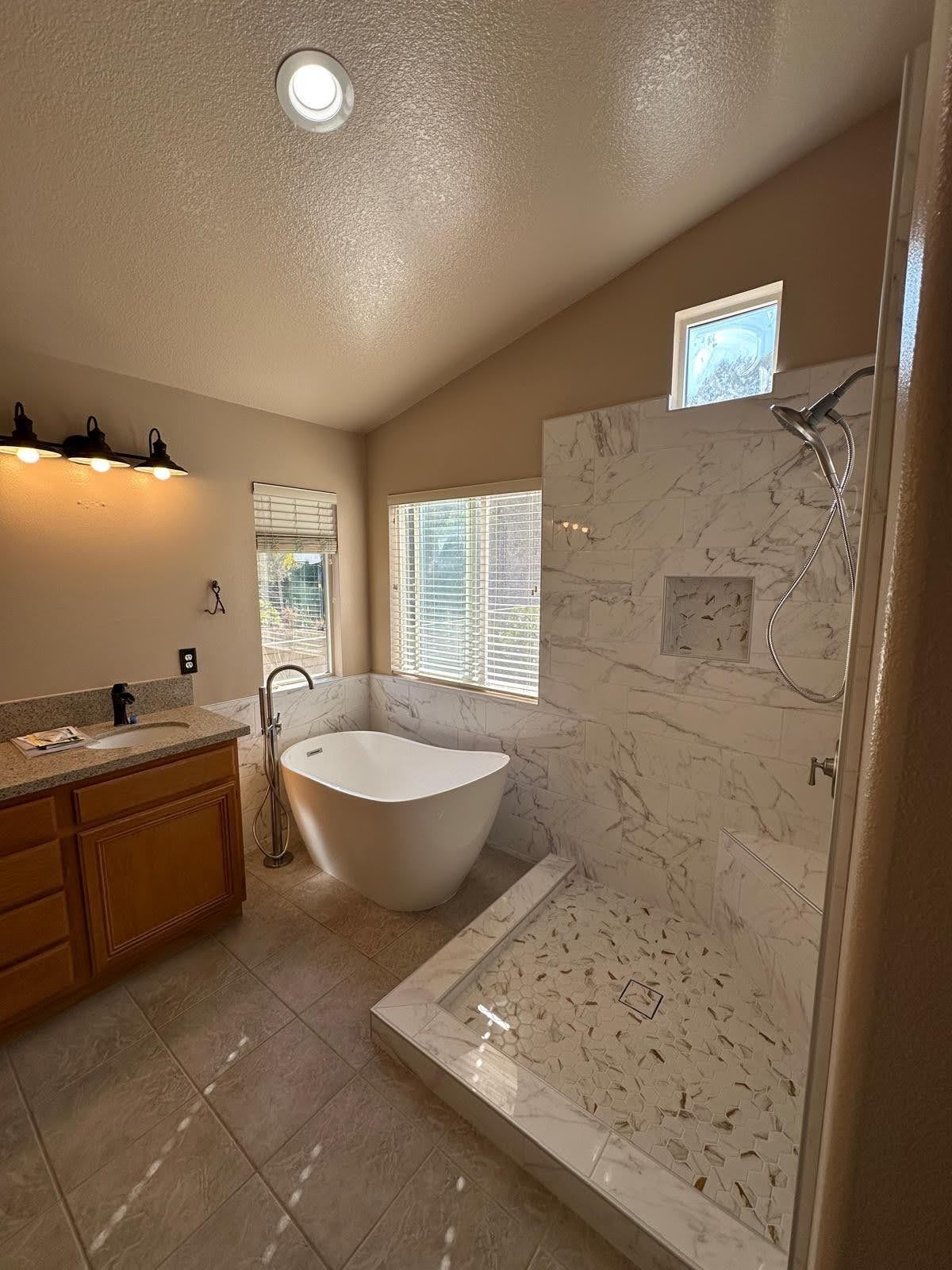 Bathroom with a large, white tub, marble shower, and wooden vanity.