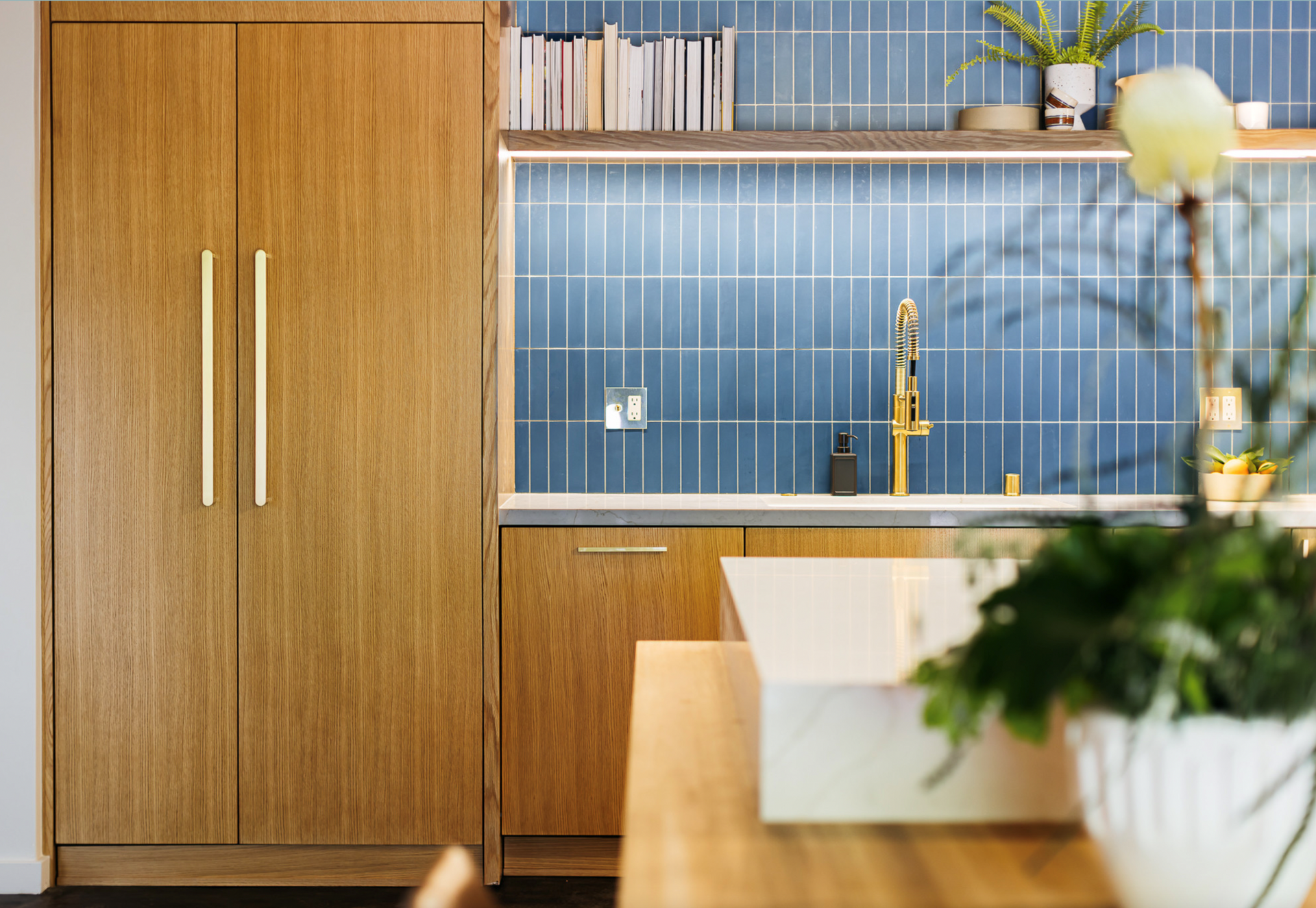 Wooden kitchen with blue tiled backsplash, gold fixtures, and a plant.