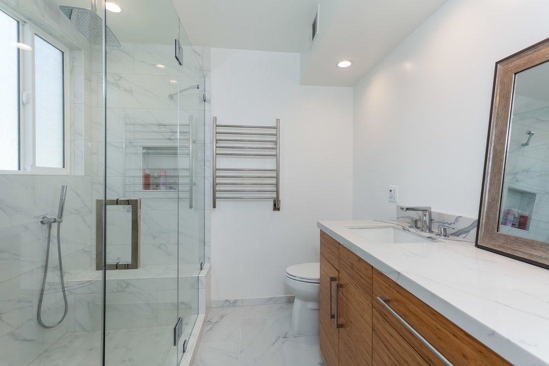 Modern bathroom with glass shower, wooden vanity, white countertop, and marble tile floor.