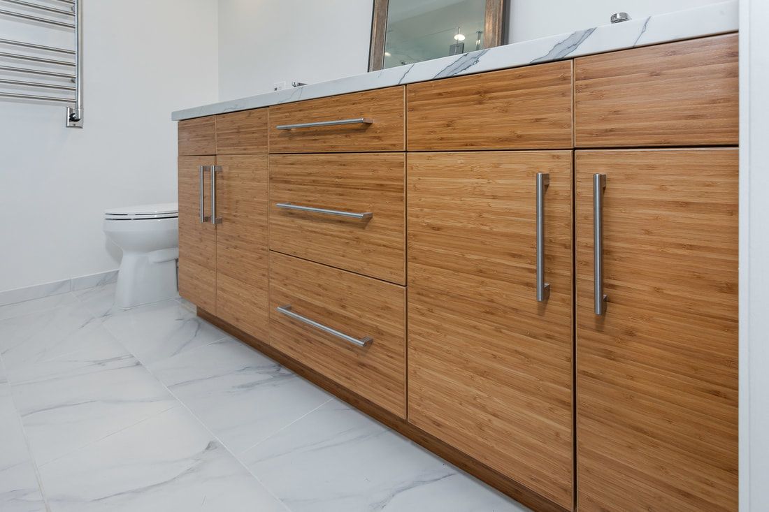 Wooden bathroom vanity with marble countertop, silver hardware, and white tile flooring.