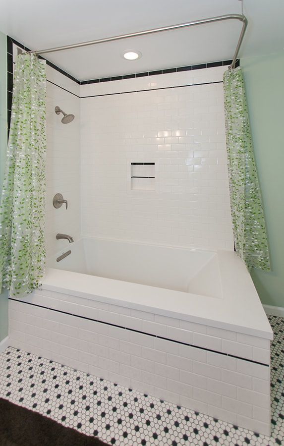 A white bathtub with black trim and green shower curtains in a bathroom with mosaic tile flooring.