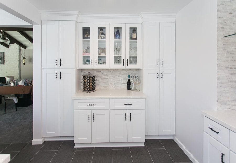 White kitchen cabinets with glass-front upper cabinets, wine rack, and countertops.