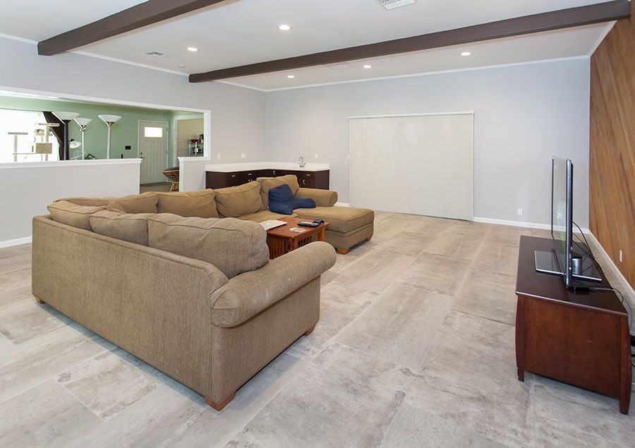 Spacious living room with sectional sofa, TV, and wooden accent wall, light gray walls and flooring.