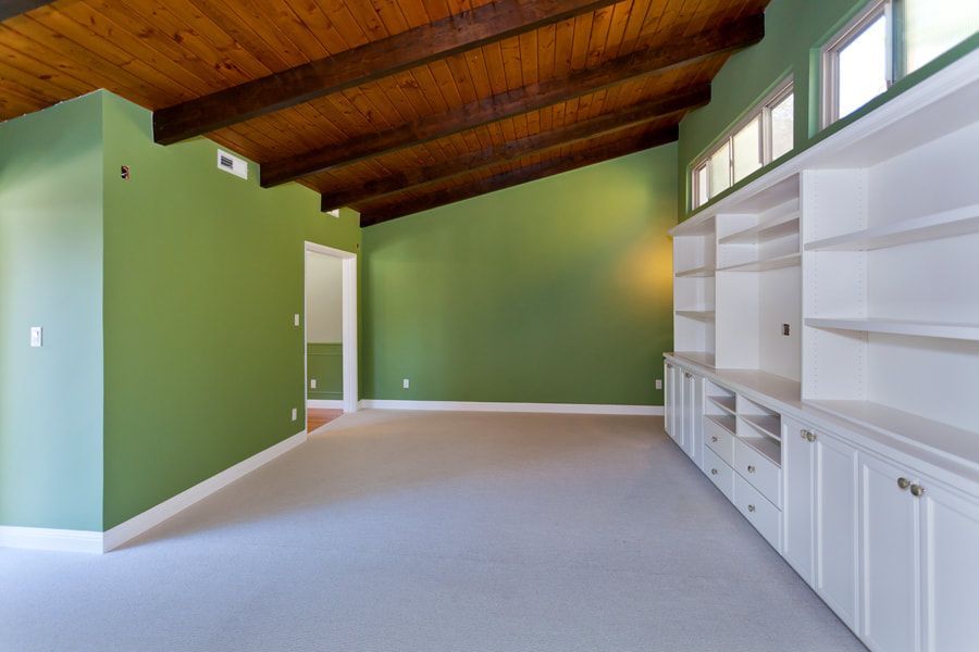 Empty room with angled green walls, wooden ceiling beams, white built-in cabinets, and light carpet.