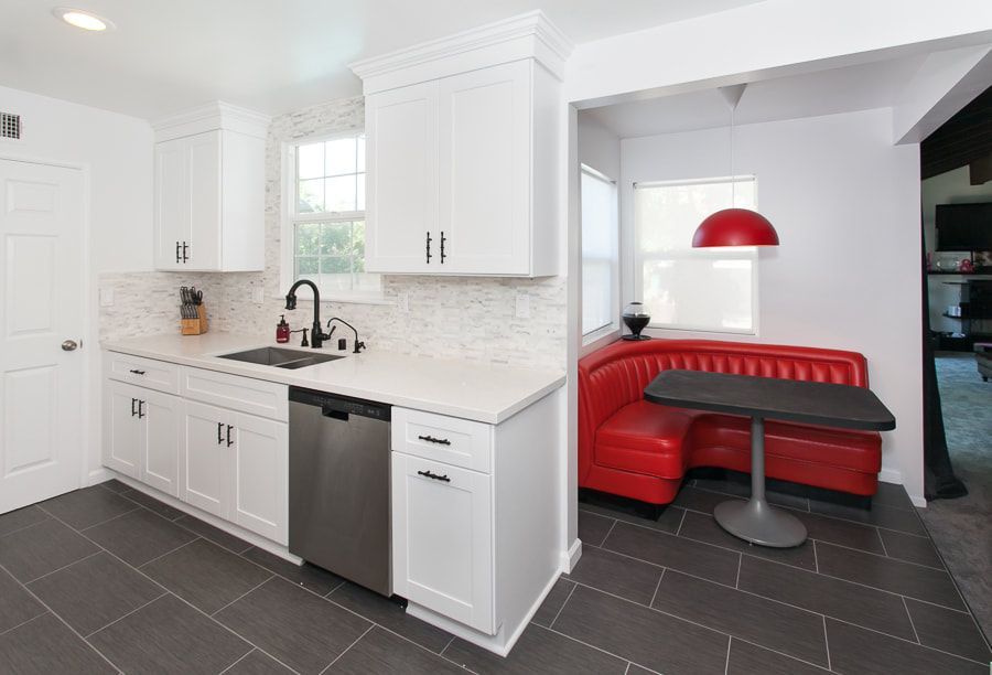 White kitchen with a red booth. Gray tiled floor, white cabinets, and stainless steel appliances.