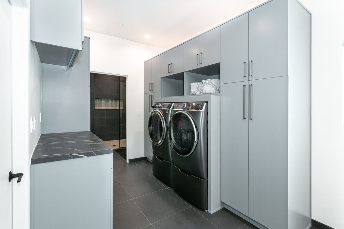 Modern laundry room with gray cabinets, appliances, and dark floor.