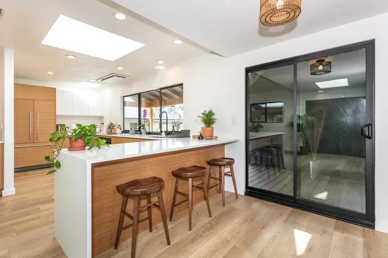 Modern kitchen with wooden island, stools, white countertops, and sliding glass door.