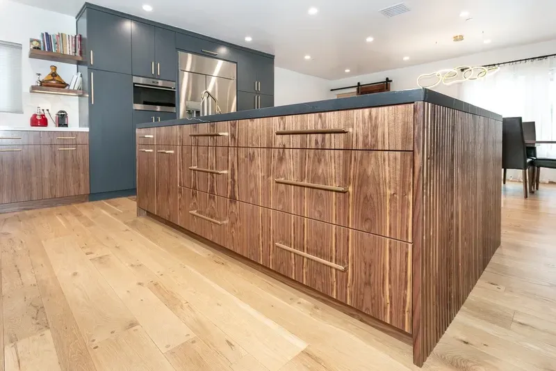 Modern kitchen with wooden island, dark cabinets, stainless steel fridge, and light wood floors.