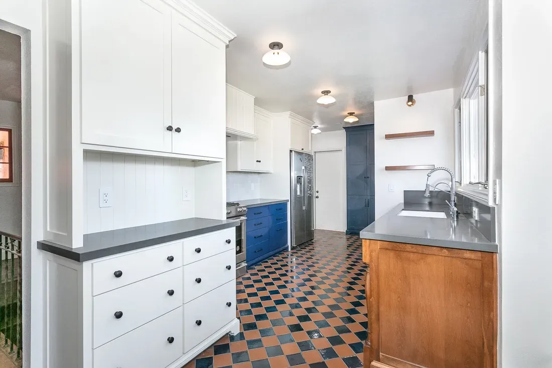 A kitchen with blue and white cabinets, checkered floor, and a stainless steel refrigerator.