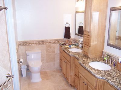 Bathroom with toilet, double sink vanity, tan tile, and a brown hand towel.