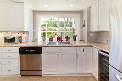 White kitchen with stainless steel appliances, a window over the sink, and beige countertops.