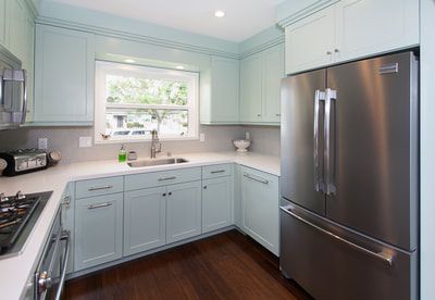 Kitchen with light blue cabinets, white countertops, stainless steel refrigerator and dark wood floors.