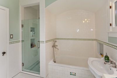 Bathroom with a white tile tub and shower. Green accents and a white sink.