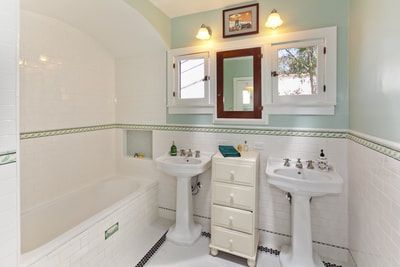 Bathroom with white tile, pedestal sinks, light blue walls, and a dark wooden cabinet.