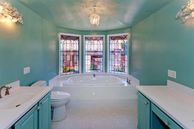 Teal bathroom with white tub, countertops, and mosaic windows.