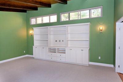 Green-walled room with white built-in storage unit, three upper windows, and sconces.