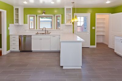 Modern kitchen with white cabinets, green walls, stainless steel appliances, and gray tile floor.
