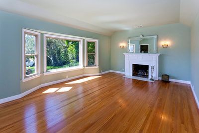 Empty living room with wood floors, fireplace, large window, and blue walls.