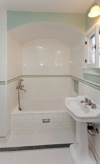 Bathroom with white tiled tub, arched alcove, pedestal sink, and green accents.
