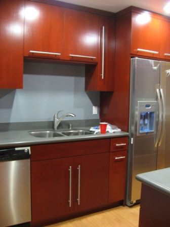 Red cabinets, stainless steel appliances in a kitchen. Gray countertop and wall.