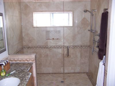 Bathroom with glass shower doors, beige tile, and granite countertop.