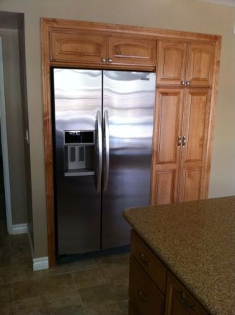 Stainless steel refrigerator flanked by wood cabinets in a kitchen setting.