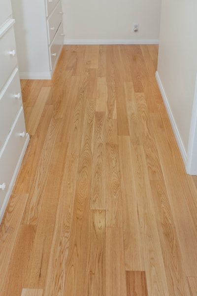 Light wood flooring in a hallway, flanked by white dressers and walls.