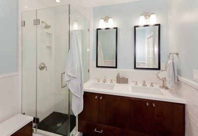 Bathroom with glass shower, double sink vanity, and light blue walls.