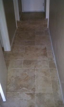 Tiled hallway with beige walls, brown tiles, and two doorways, leading to a white door at the end.