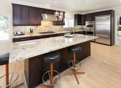 Modern kitchen with dark brown cabinets, granite island, and stainless steel appliances.