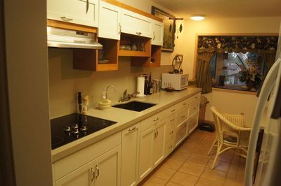 Kitchen with white cabinets, black stovetop, small dining area, and window.