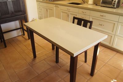 A dining table with one chair in a kitchen, with cabinets, a counter, and tile flooring.